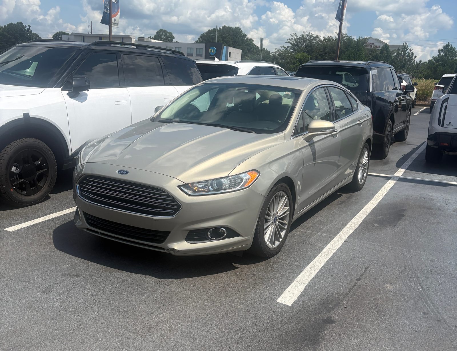 A gold 2015 Ford Fusion SE from the Seven Fleet Group fleet, front three-quarter view